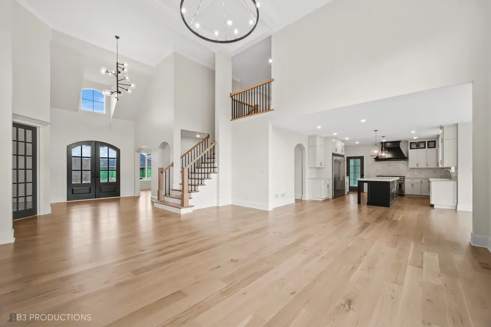 Two-story entry foyer with an arched front door, an oak staircase with black iron balusters, and an open view through to the kitchen