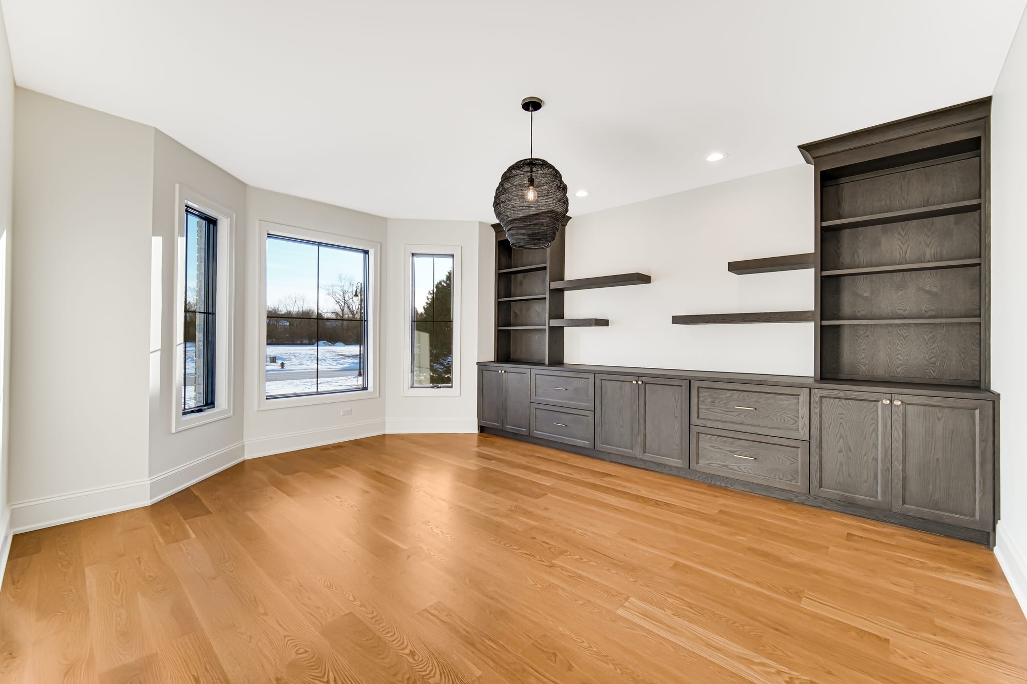 Study with built-in gray oak shelving and a bay window onto the yard