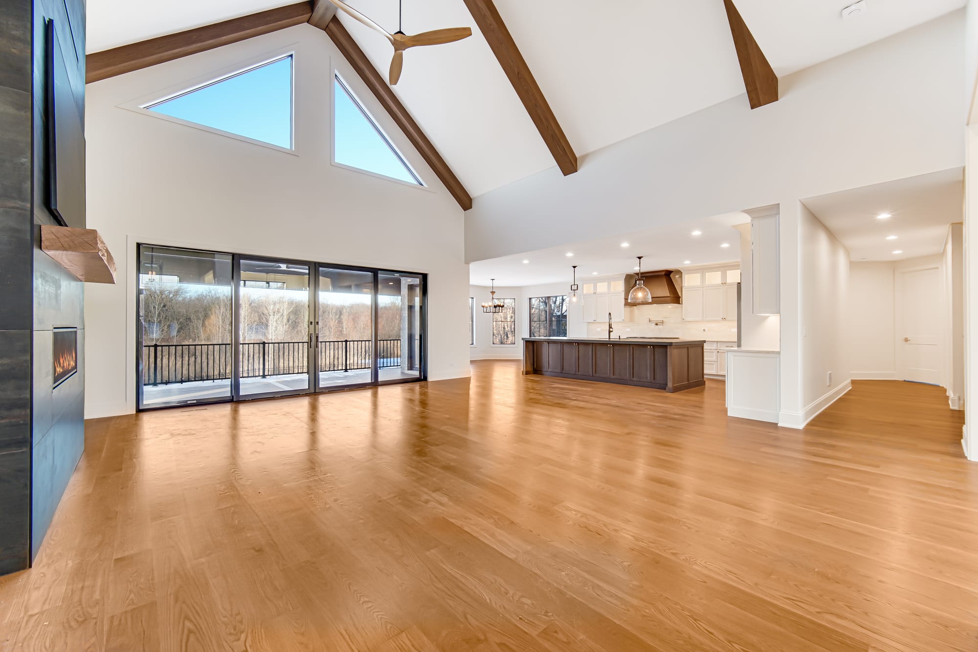Vaulted great room with exposed wood beams, a linear fireplace, and sliding doors onto a deck
