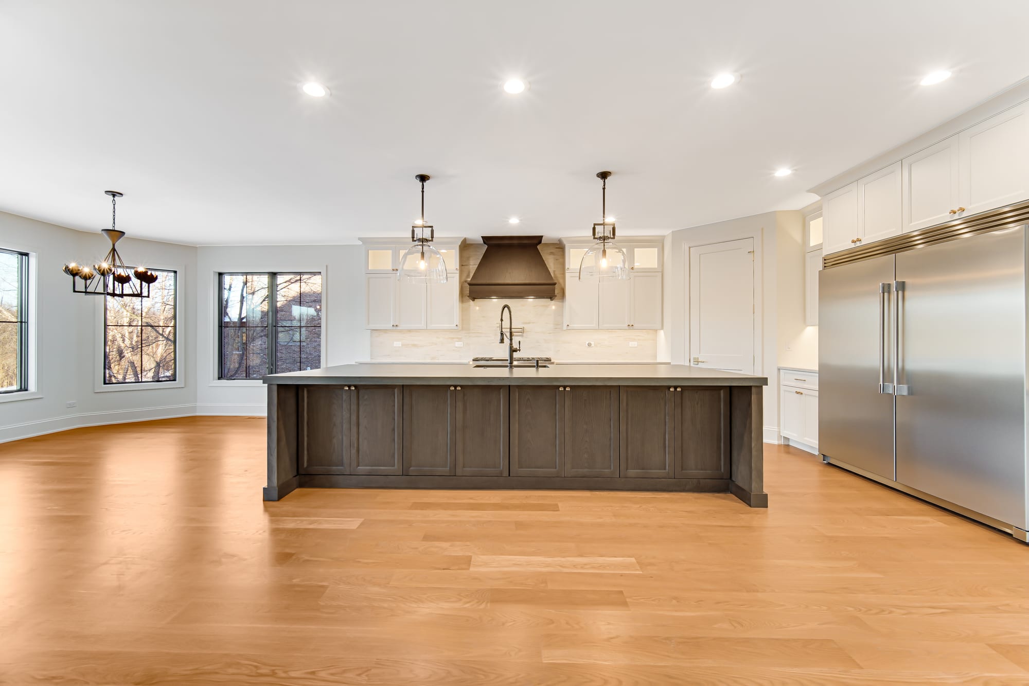 Kitchen with a dark stained island, brass pendant lighting, and a custom wood range hood