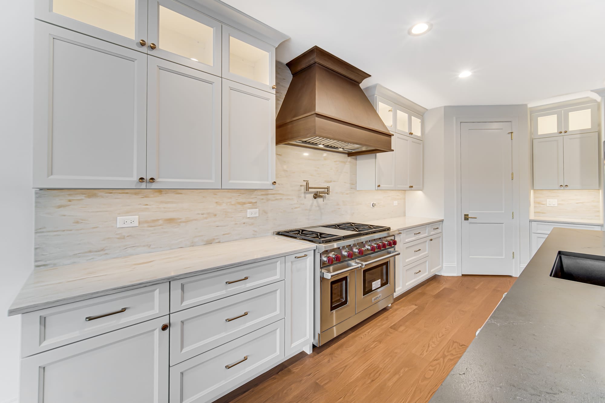 Professional range beneath a custom wood hood against a marble backsplash