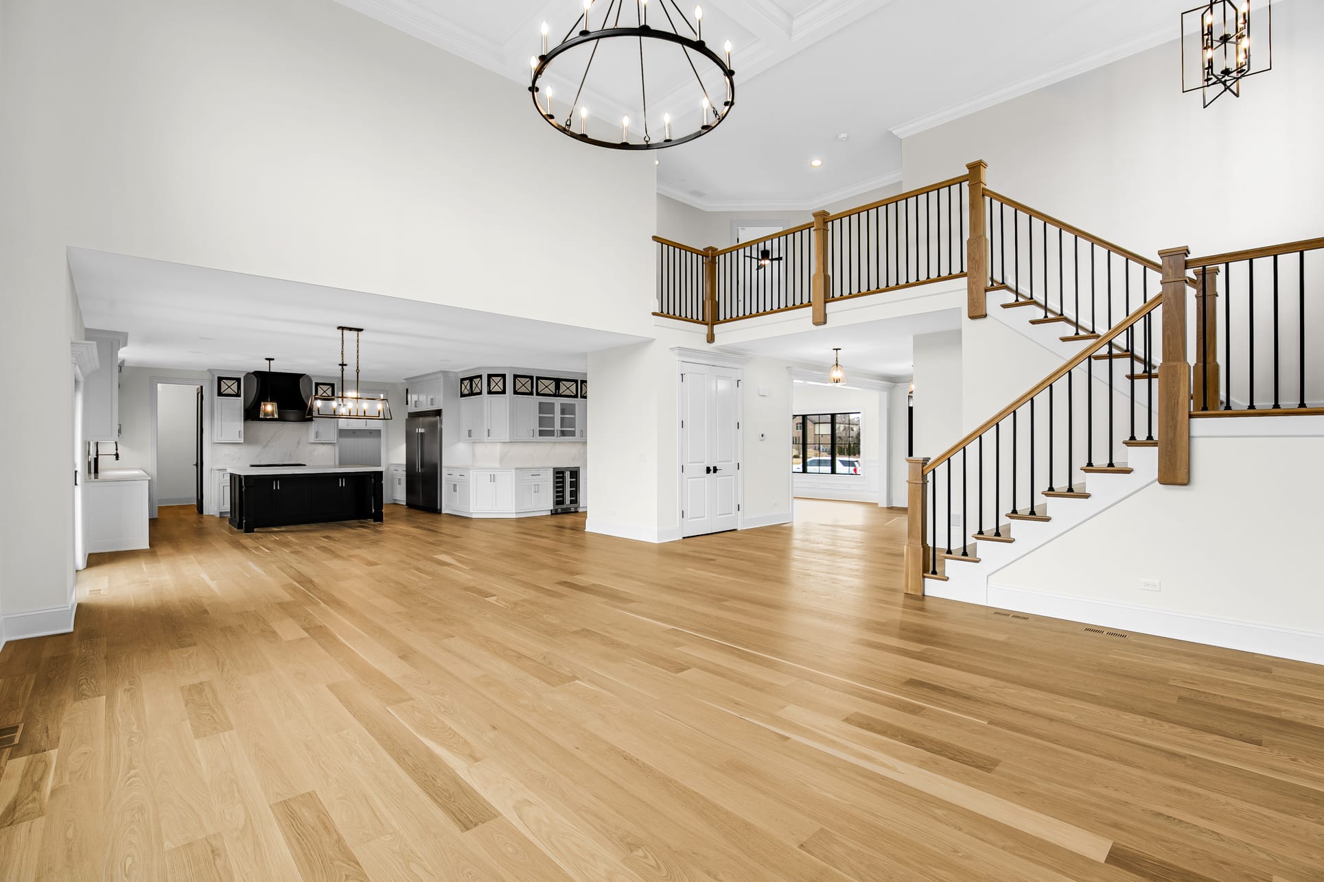 Two-story great room with an iron ring chandelier beside an open oak staircase