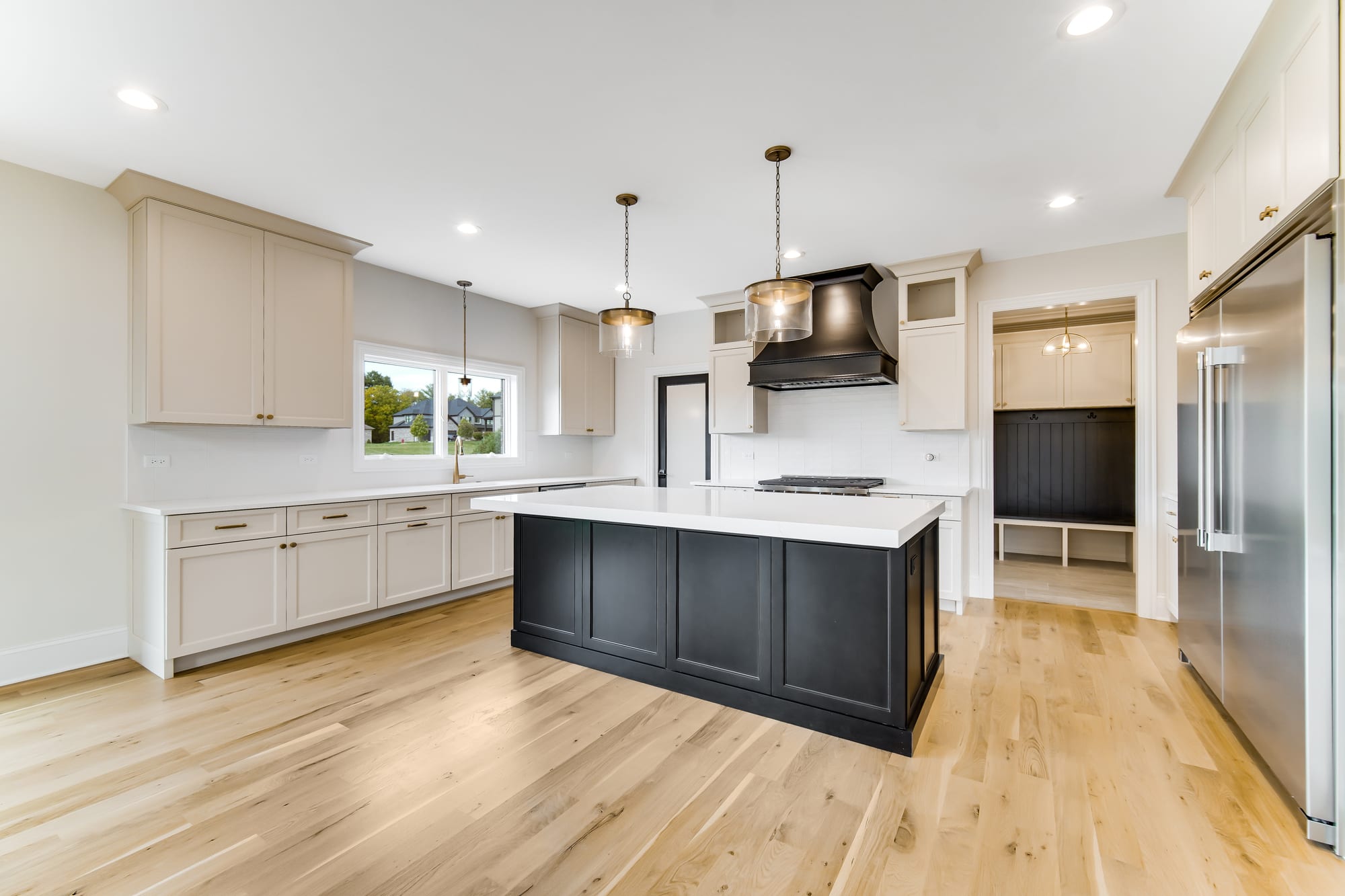 Kitchen with a black island, brass pendants, and a walk-through mudroom beyond